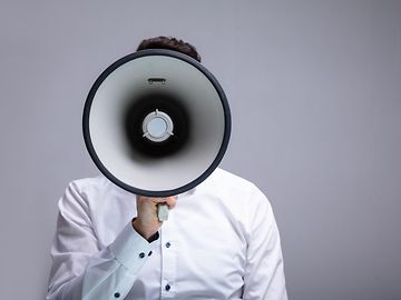 Man holding large megaphone covers his face