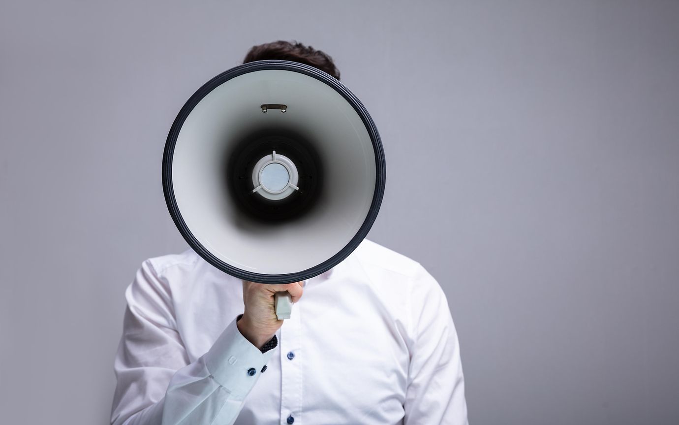 Man holding large megaphone covers his face